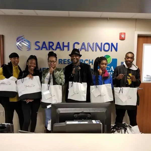 Six volunteers holding Glendra’s Love tote bags at the Sarah Cannon front desk