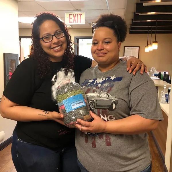 Two women smiling and holding a bag of crocheted hats with a donation label